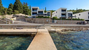 A modern building with multiple balconies, a clear pool area, and a stone staircase leading to a higher level. - Cozy apartment in Omisalj with house sea view (Omisalj)
