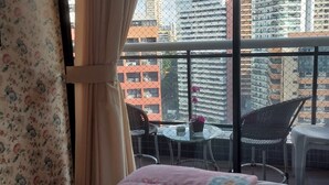 Un balcón con una cama, una mesa con sillas y vistas a edificios altos.