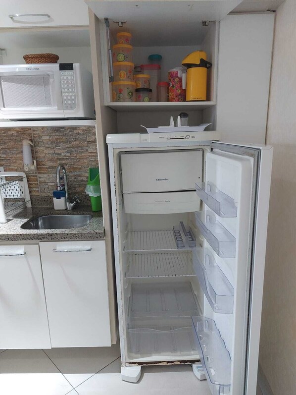 A kitchen with a microwave, sink, and a refrigerator with shelves.