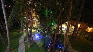 Ein angelegter Garten mit Wasserspiel, Palmen und einem Gebäude mit beleuchteten Fenstern.
