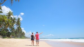 Ein Paar spaziert über einen Sandstrand, im Hintergrund Palmen und das Meer.