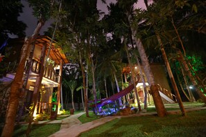 A well-lit outdoor area with a slide, palm trees, and a building with multiple levels and balconies.