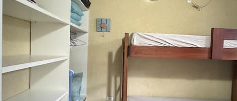 A room with a bunk bed, a white wardrobe, and a shelf unit.