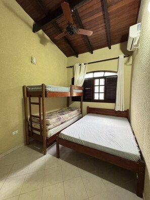 A room with two bunk beds, a ceiling fan, a window with curtains, and a wall-mounted air conditioner. - House in gated community beachfront - sleeps 8 - weekends/seasonal rental (São Sebastião)