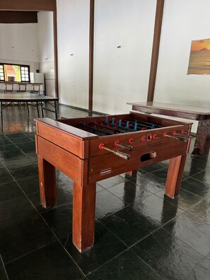 A wooden foosball table in a room with tiled flooring and a large window.