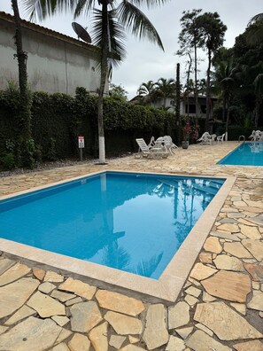 Una piscina rectangular amb un marc de pedra, rodejada de gandules i palmeres.