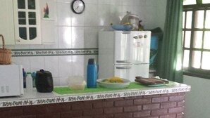 A kitchen with a tiled backsplash, a refrigerator, a clock, and a window with curtains. - House in gated community beachfront - sleeps 8 - weekends/seasonal rental (São Sebastião)