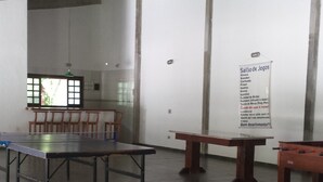 A spacious room with a high ceiling, a long table, several chairs, and a sign listing available games. - House in gated community beachfront - sleeps 8 - weekends/seasonal rental (São Sebastião)