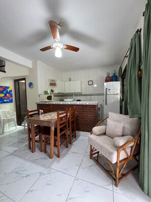 A compact kitchen with a dining area, a ceiling fan, a refrigerator, and a green curtain.