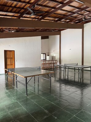 Una habitació àmplia amb una taula de ping-pong, una porta de fusta i una cuina al fons.