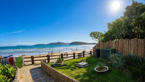 A beach view with a wooden fence, a grassy area with plants, and a clear sky.