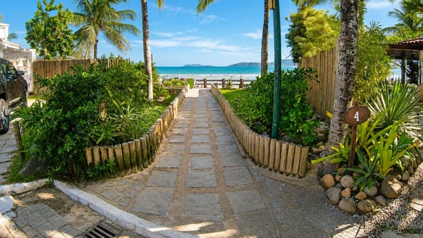 A paved pathway leading to a beach with palm trees and a clear blue sky.