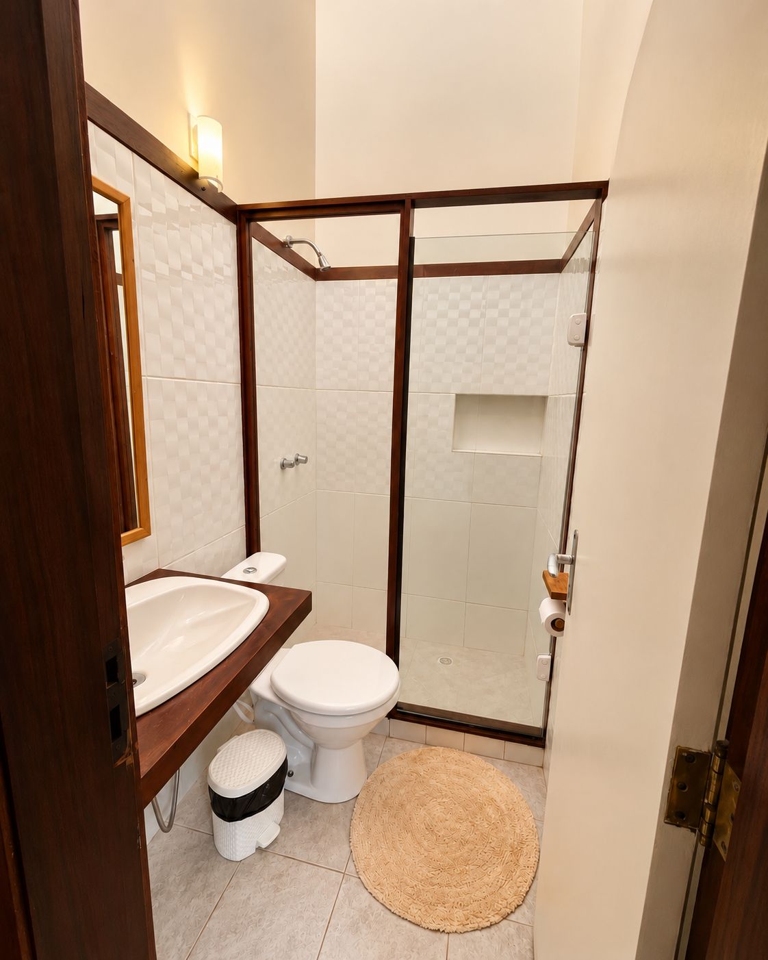Un baño con tocador de madera, inodoro, cabina de ducha y alfombra redonda.