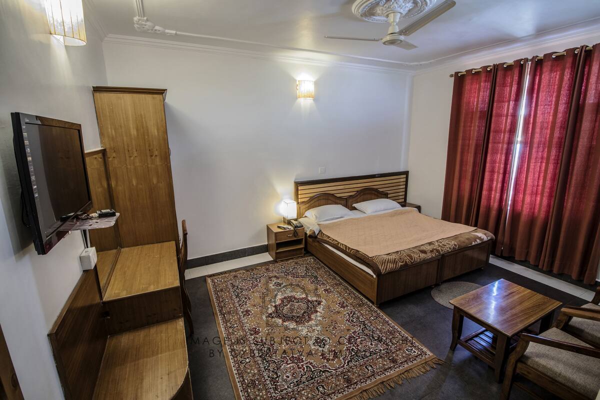 Una camera d'albergo con un letto, una scrivania, una sedia, una televisione, un armadio e una ventola a soffitto.