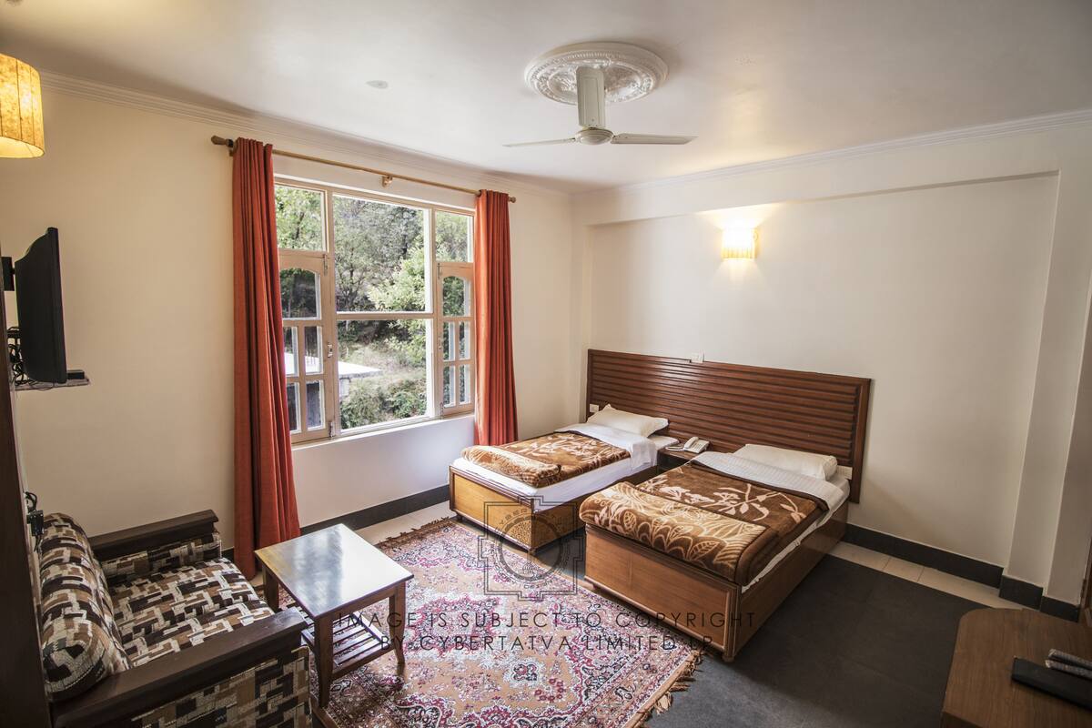 Camera d'albergo con due letti, un divano, un tavolino e un'ampia finestra con tende.