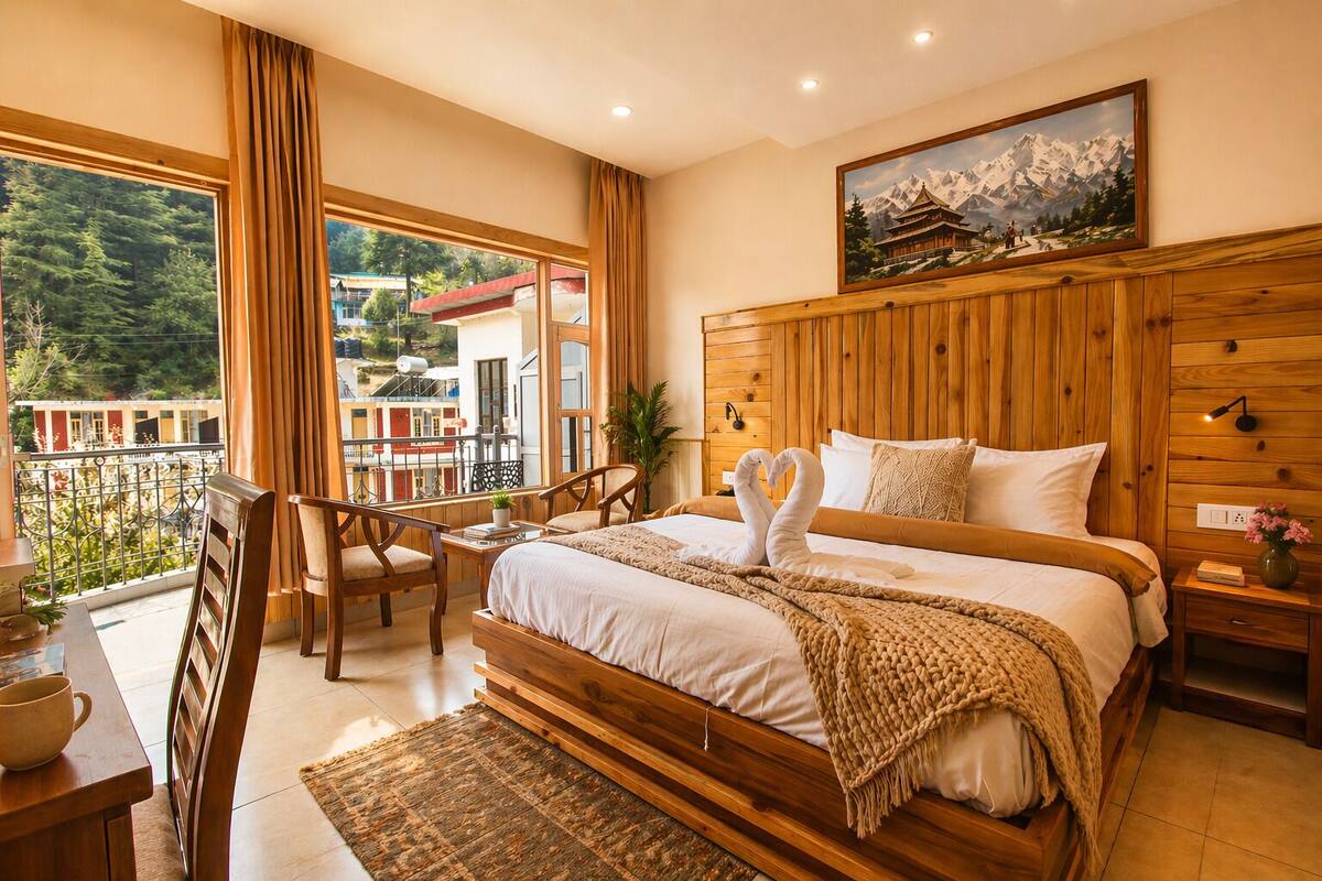 Una camera da letto con testiera in legno, un letto con lenzuola bianche, un balcone con vista sugli edifici e un quadro raffigurante montagne.