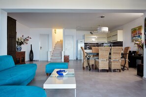 Relax in this airy living space with a comfortable sofa, dining area, and kitchen in the background.