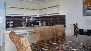 A modern kitchen with white cabinets, a microwave, and a coffee maker. There is a dining table with a floral tablecloth and woven chairs. - Luxurious Villa in Apostolata 5★ resort, 3BR, sea views, free parking! (Skala)