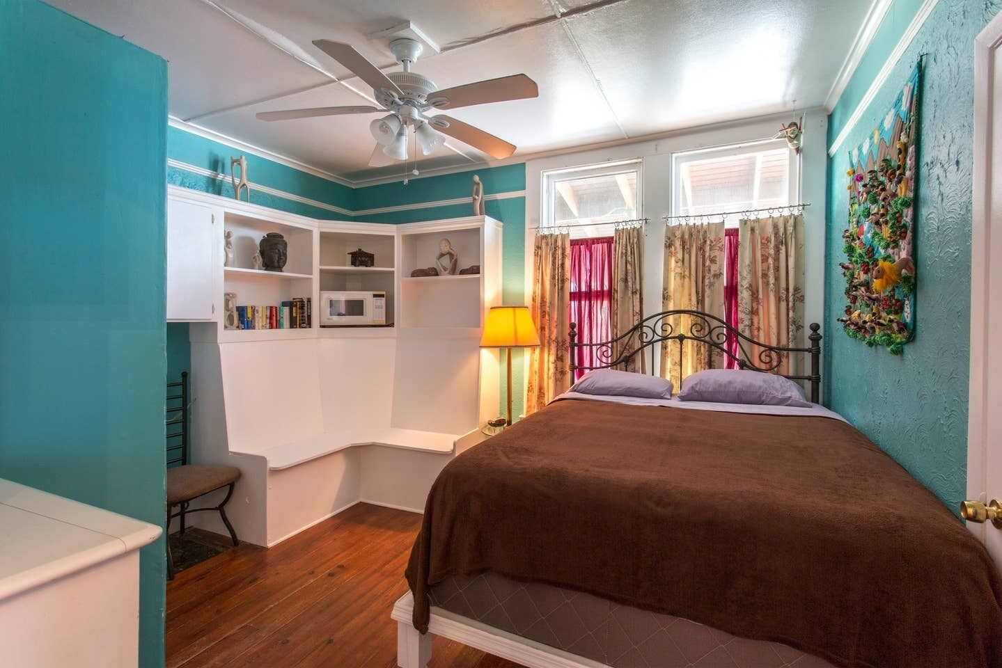 Un dormitorio con cama, ventilador de techo, armario, lámpara y ventana con cortinas.