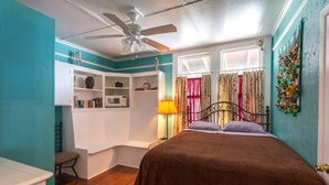 Une chambre à coucher avec un lit, un ventilateur de plafond, une armoire, une lampe et une fenêtre avec des rideaux.