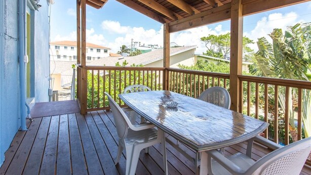 Une terrasse en bois avec une table et des chaises, donnant sur un quartier résidentiel avec des maisons et de la verdure.