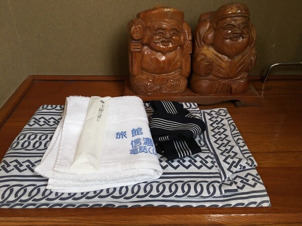 A neatly folded white towel and a black and white patterned towel on a bed with a geometric patterned bedspread.