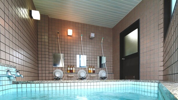 A swimming pool with a tiled floor and a tiled wall. There are two faucets and two showerheads on the wall. - Nanakurasou (Omachi)