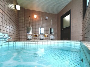 A swimming pool with a tiled floor and a tiled wall. There are two faucets and two showerheads on the wall.
