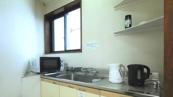 A small kitchenette with a microwave, sink, and tea pot.