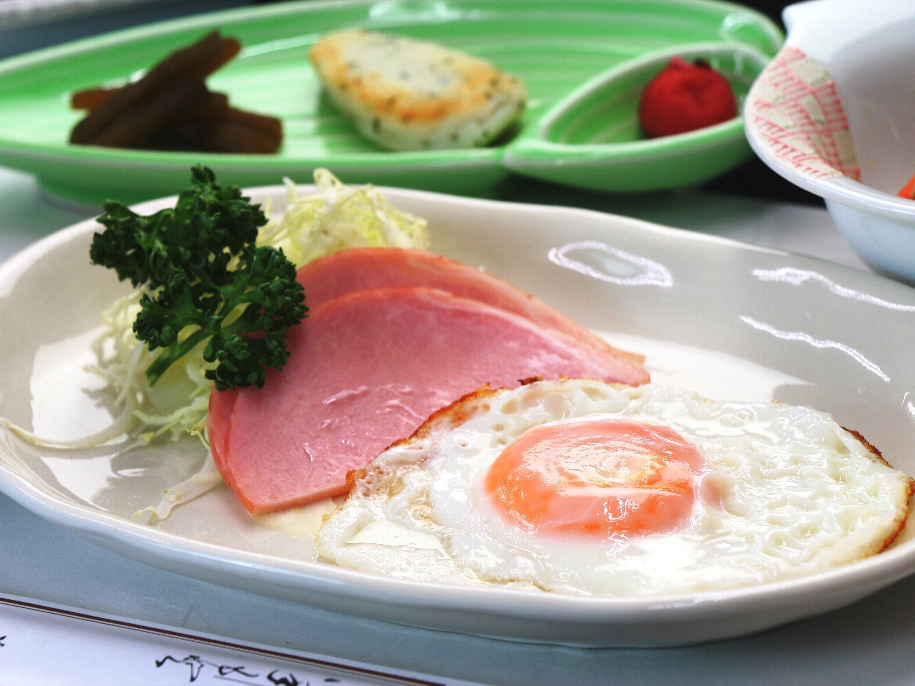 A plate with ham, a fried egg, and some vegetables.
