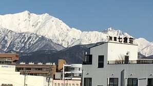 A building with a sign in a foreign language, surrounded by snow-capped mountains. - Nanakurasou (Omachi)