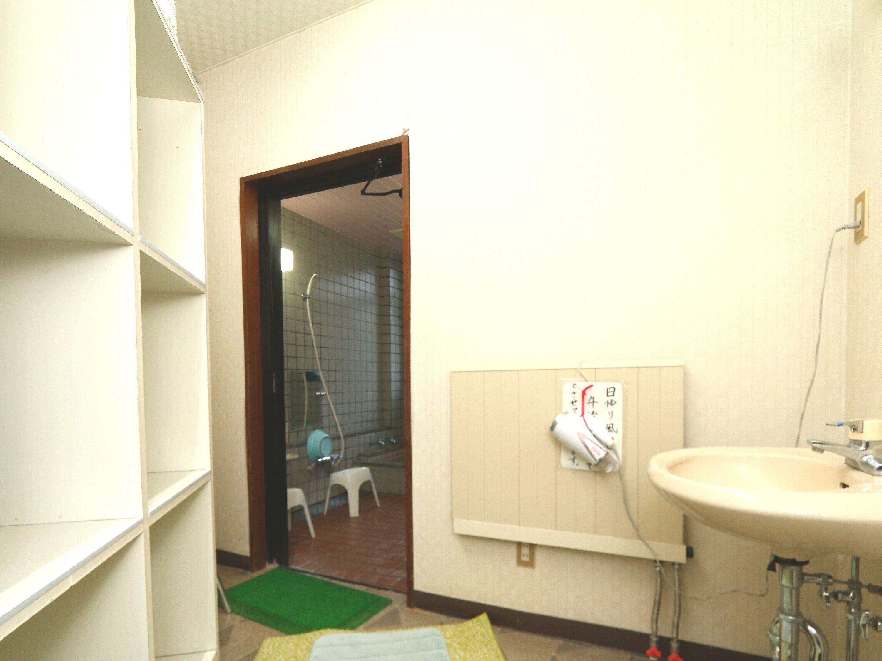 A bathroom with a sink, mirror, and a towel rack. There is a green mat on the floor and a white door leading to a shower area.