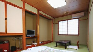 A traditional Japanese-style room with tatami flooring, a bed with a floral bedspread, a television on a low shelf, and a sliding door. - Nanakurasou (Omachi)