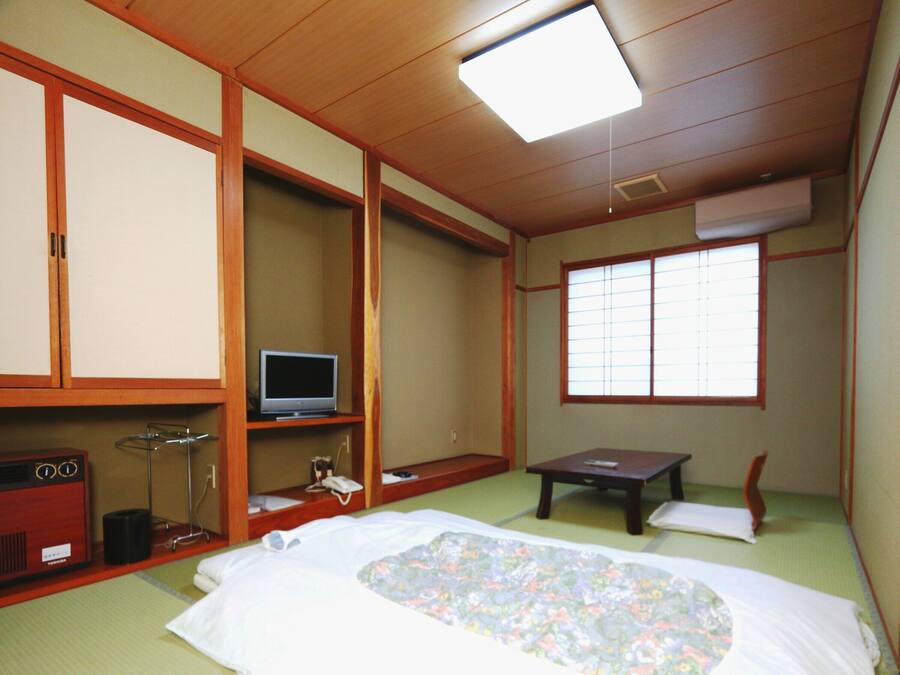 Habitació japonesa tradicional amb sòcols de tatami, un llit amb col·cha floral, una televisió sobre una estant baixa i una porta corredissa.