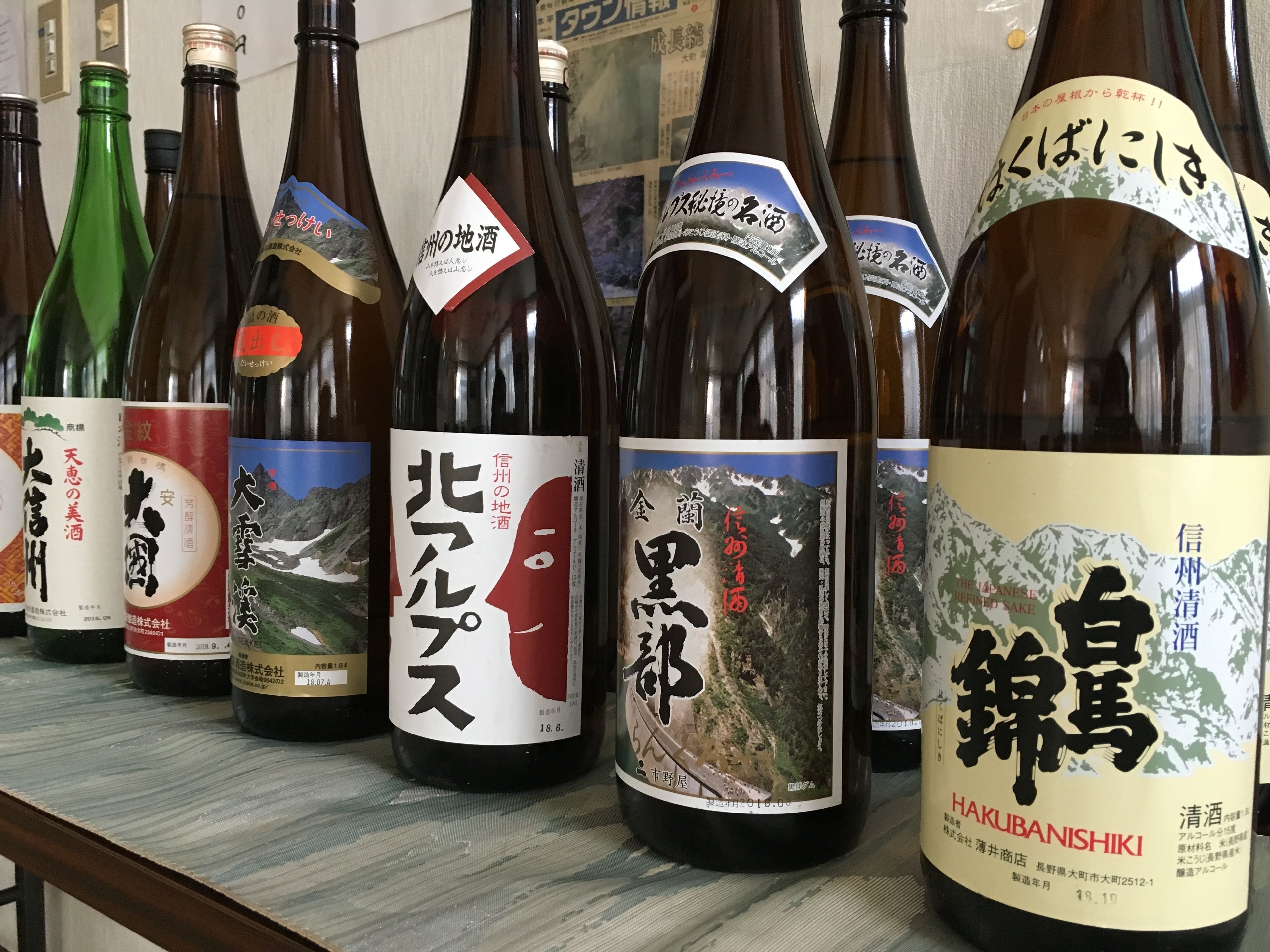 Une rangée de bouteilles de bière, toutes étiquetées, chacune présentant un paysage de montagne et du texte en japonais.