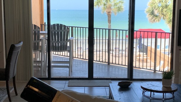 Ein Zimmer mit Meerblick, ein Balkon mit Stühlen und eine Weinflasche auf einem Tisch.