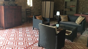 Una sala de estar acogedora con muebles de mimbre, un tapete estampado, una pared de piedra y un mueble de madera.
