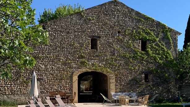Un edificio de piedra con piscina, mobiliario exterior y cielo despejado.