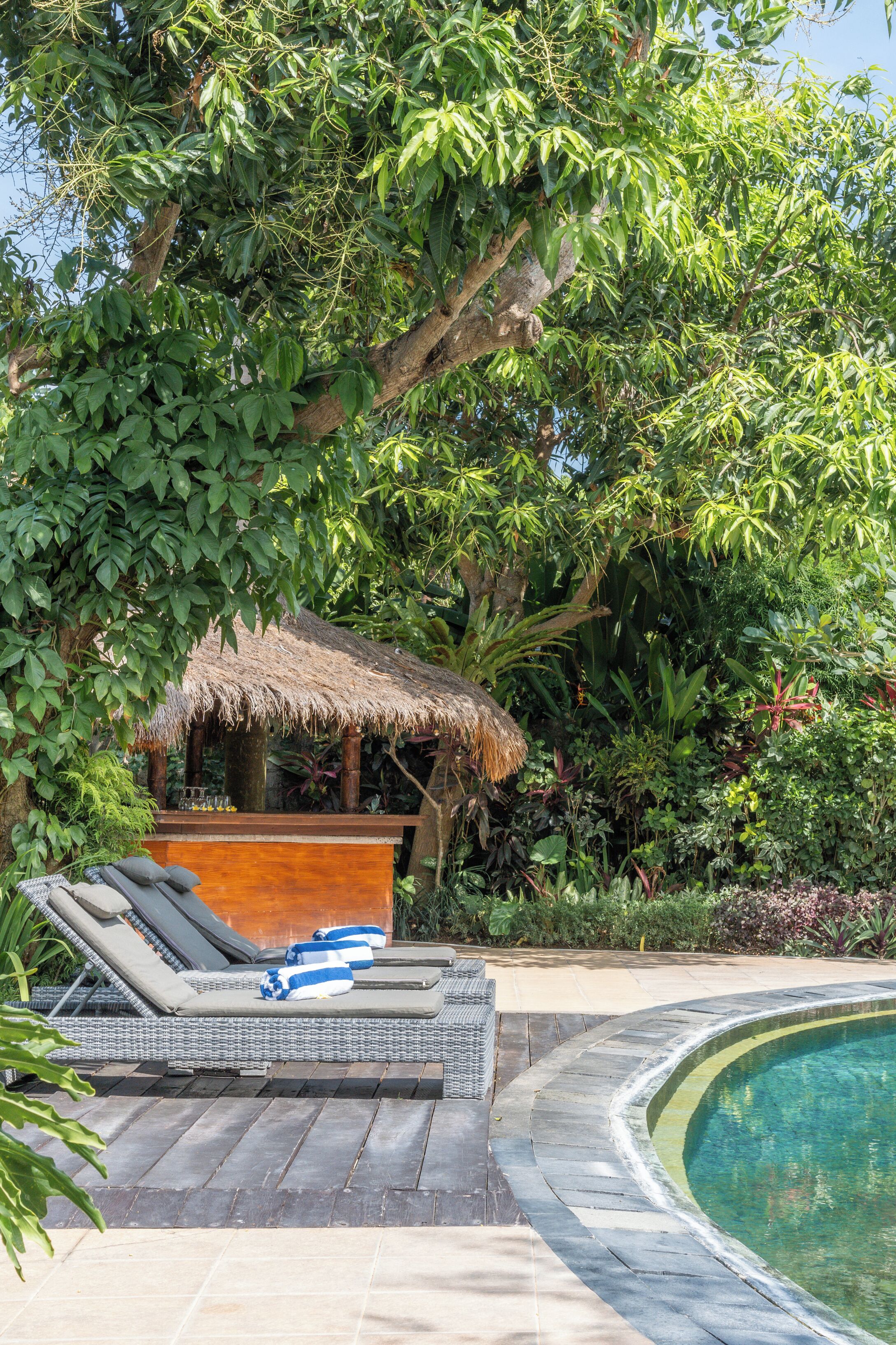 A poolside area with lounge chairs, a thatched-roof structure, and lush greenery.