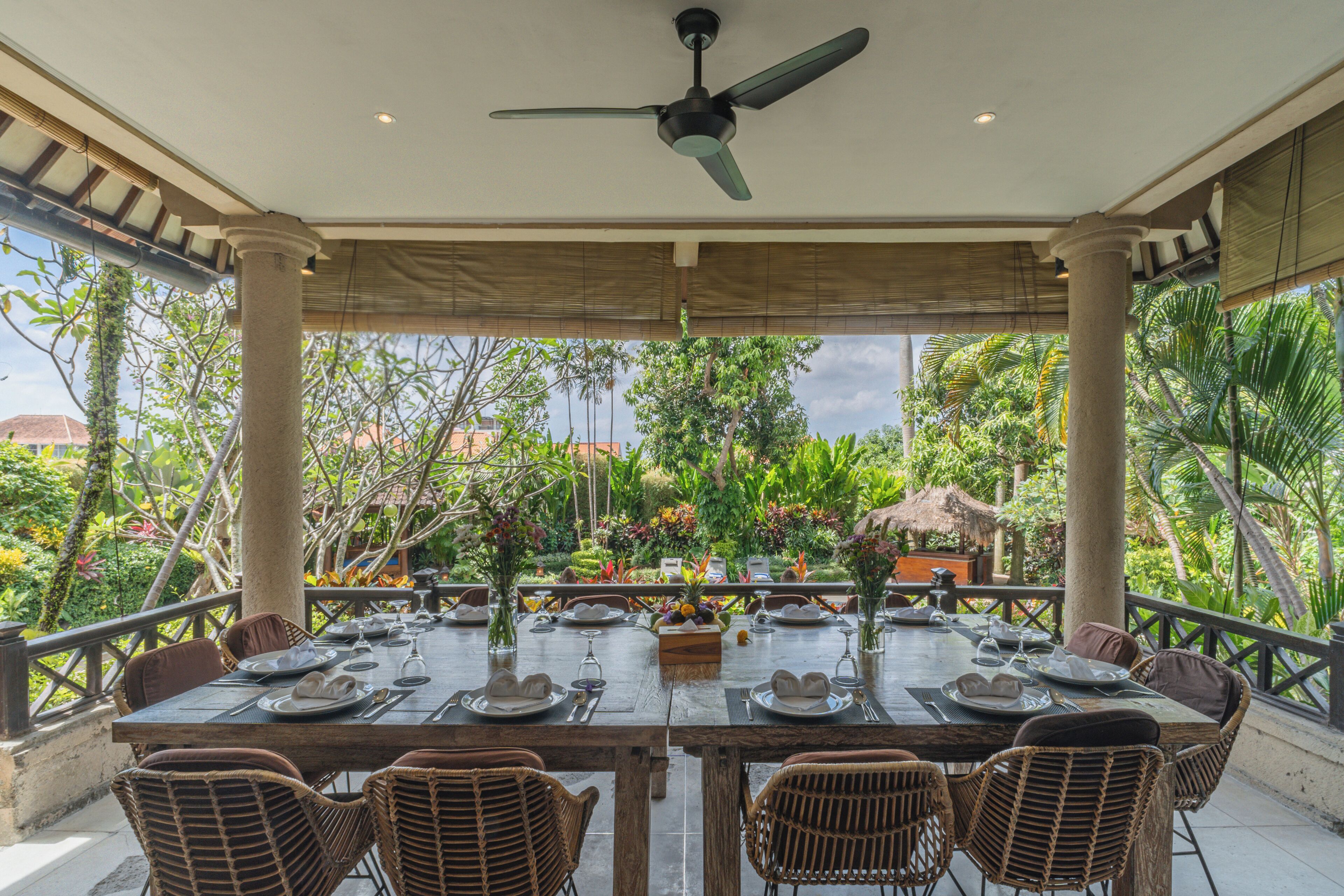 An outdoor dining area with a table set for four, surrounded by wicker chairs, under a ceiling fan.