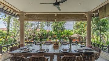 An outdoor dining area with a table set for four, surrounded by wicker chairs, under a ceiling fan.