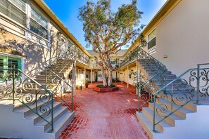 Stroll through the serene courtyard, surrounded by a tree and a brick pathway, and ascend to the entrance via ornate metal railings.