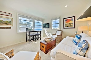 A living room with a white sofa, a dining table with chairs, a TV, and a view of the outdoors.