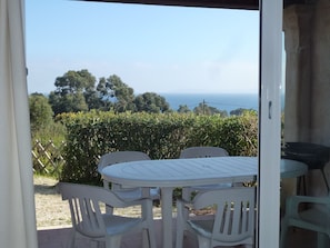 An outdoor patio with a table and chairs, a view of the sea, and a hedge in the background. - Apartments: 2 cabin rooms on the ground floor for 2/6 people (Le Lavandou)