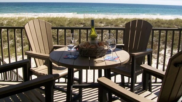 A wooden deck with a round table and four Adirondack chairs, overlooking a beach with the ocean in the background. - Turtle's Nest-Gulf Front Home w/Gorgeous Furnishings. Sleeps 10 (Navarre)