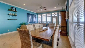 A dining area with a wooden table and wicker chairs, a ceiling fan, and a view through large windows. - Turtle's Nest-Gulf Front Home w/Gorgeous Furnishings. Sleeps 10 (Navarre)