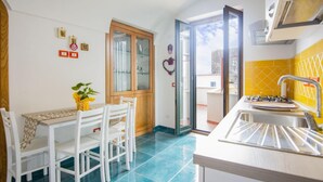 A compact kitchen with a dining table, chairs, a small island with a sink, and a sliding glass door leading to a balcony.