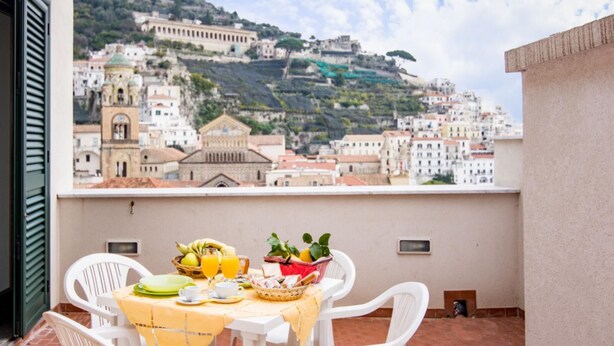 A balcony with a table set for breakfast, overlooking a hillside town with historic buildings.