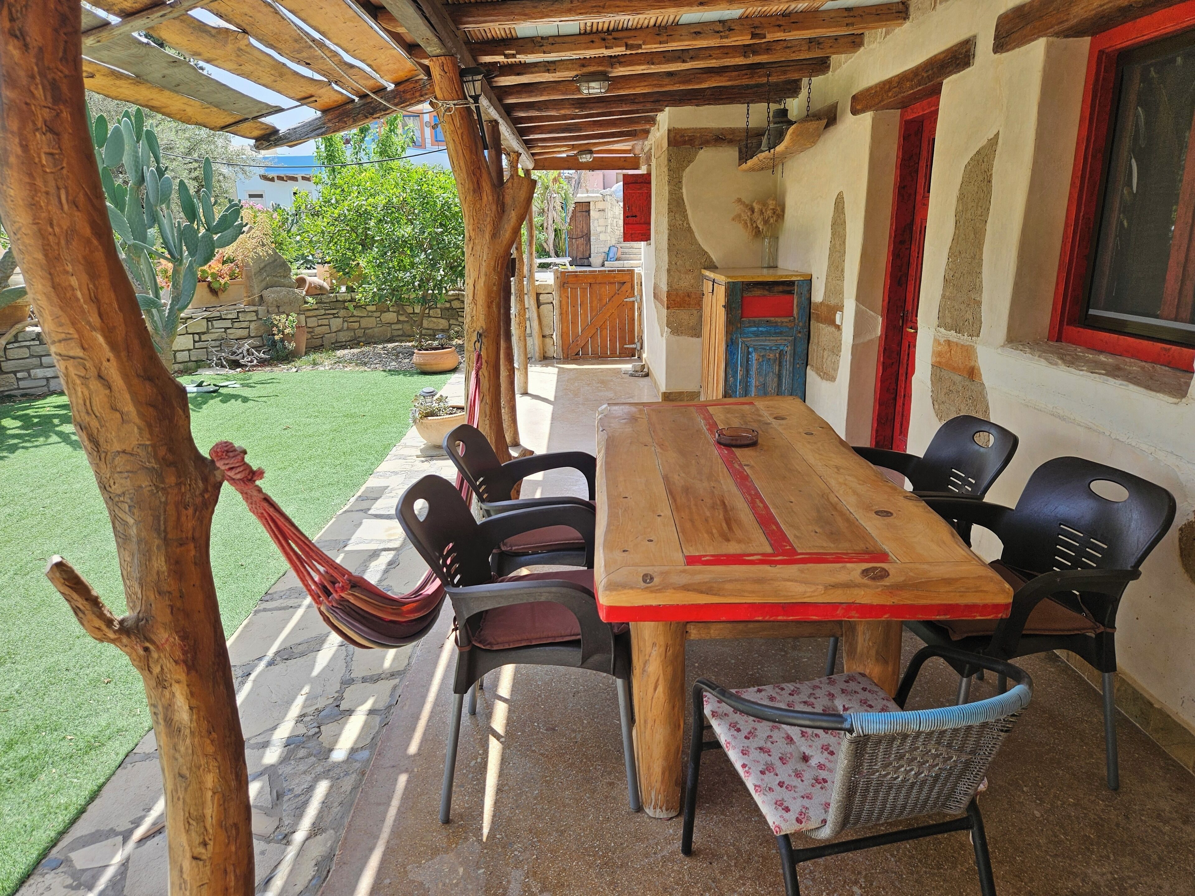 Una mesa de madera con sillas, una hamaca y un camino de piedra que lleva a un edificio.