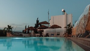 A swimming pool with lounge chairs and umbrellas, a building with a satellite dish, and a rocky landscape in the background. - Villa Kokkino Skufitza,charming holiday home made of clay, pool, private garden (Pitsidia)